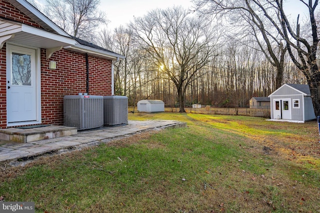 view of yard with a storage unit, an outbuilding, central AC, and fence