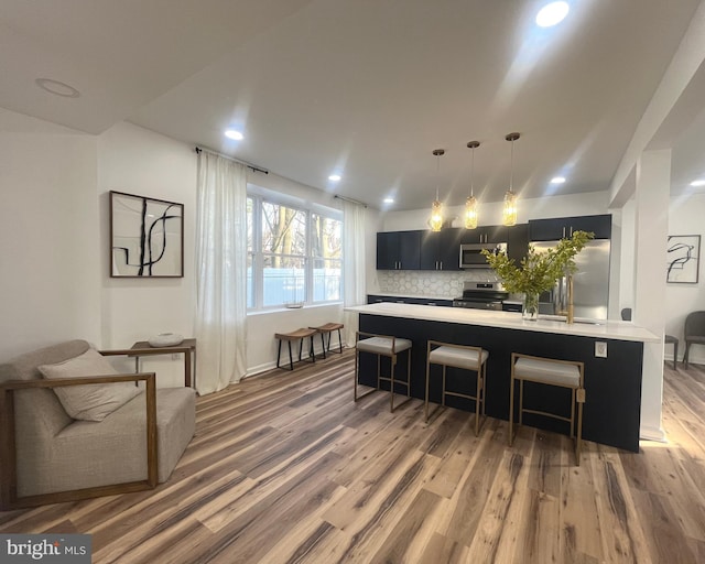 kitchen with wood finished floors, a breakfast bar, stainless steel appliances, light countertops, and dark cabinets