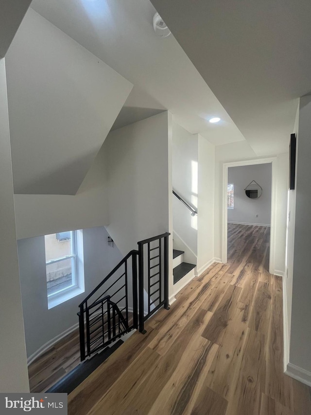 corridor with an upstairs landing, baseboards, and wood finished floors