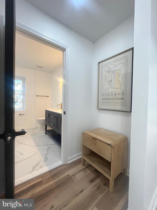 hallway featuring light wood finished floors, visible vents, baseboards, and a sink