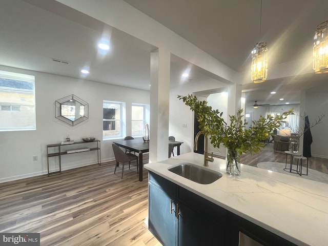 kitchen featuring a sink, decorative light fixtures, light wood-style floors, light stone countertops, and ceiling fan