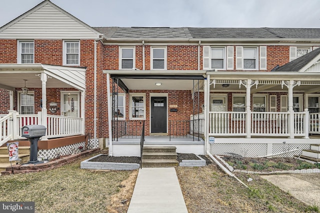 townhome / multi-family property featuring brick siding, covered porch, and roof with shingles