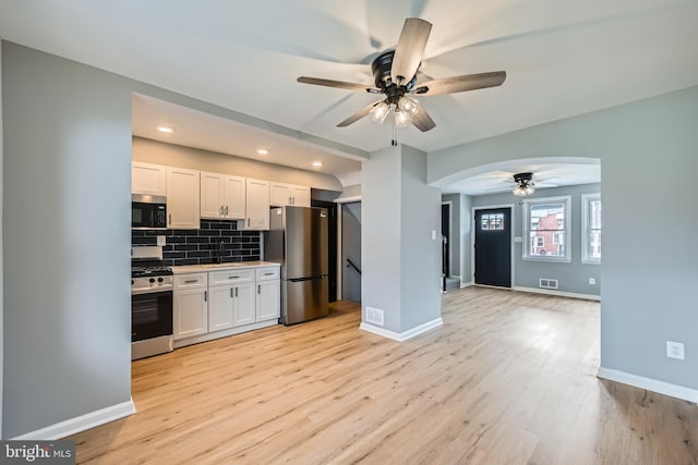 kitchen featuring a ceiling fan, stainless steel appliances, arched walkways, white cabinets, and decorative backsplash