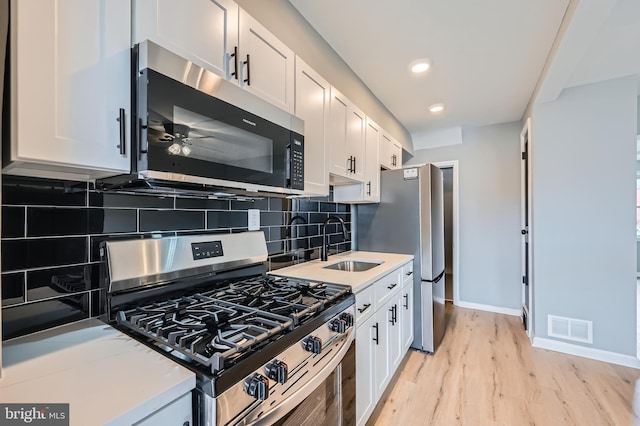 kitchen with visible vents, light wood-style flooring, a sink, stainless steel appliances, and white cabinets