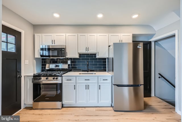 kitchen with light wood-style flooring, a sink, light countertops, appliances with stainless steel finishes, and tasteful backsplash