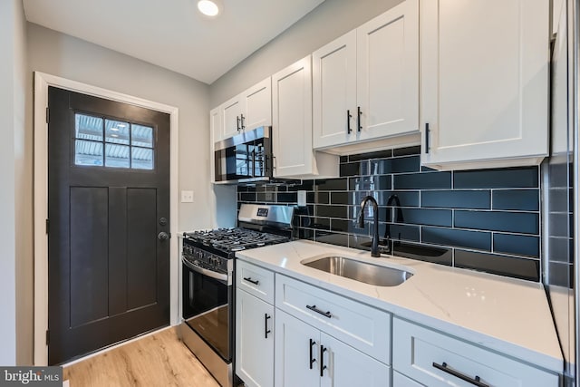 kitchen with light stone countertops, a sink, decorative backsplash, stainless steel appliances, and white cabinetry