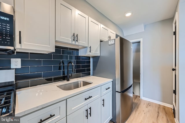 kitchen featuring tasteful backsplash, light stone counters, appliances with stainless steel finishes, white cabinets, and a sink