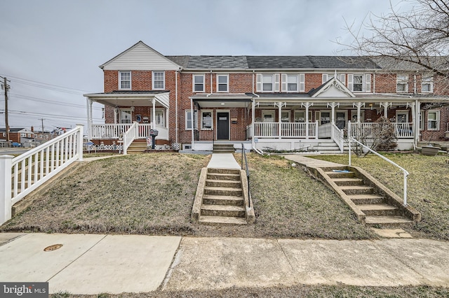 townhome / multi-family property with a front lawn, stairway, brick siding, and covered porch