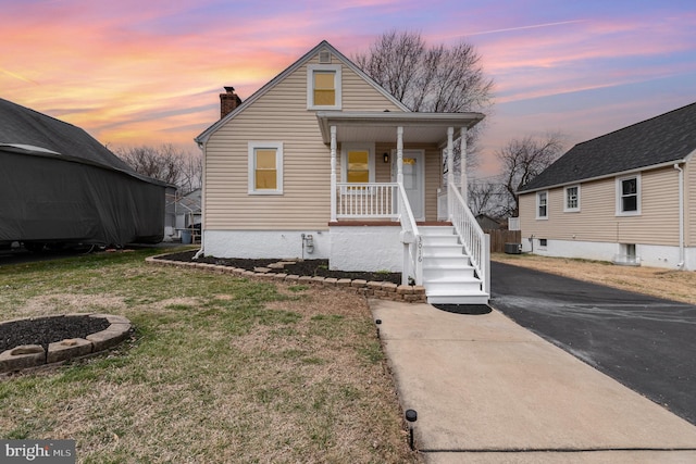 bungalow-style house featuring a lawn, a porch, an outdoor fire pit, cooling unit, and a chimney