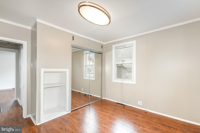 unfurnished bedroom featuring crown molding, wood finished floors, a closet, and baseboards