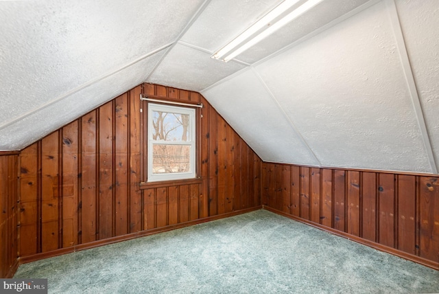 bonus room featuring wood walls, a textured ceiling, lofted ceiling, and carpet floors