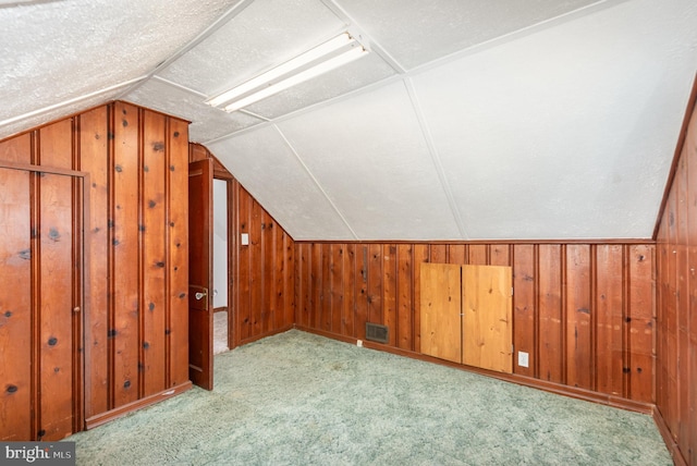 additional living space with visible vents, wood walls, lofted ceiling, and carpet floors