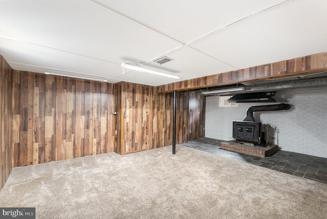 finished basement with visible vents, wooden walls, a wood stove, and carpet