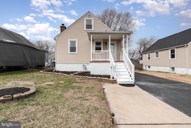 bungalow-style home featuring central AC unit, an outdoor fire pit, a porch, a chimney, and a front lawn