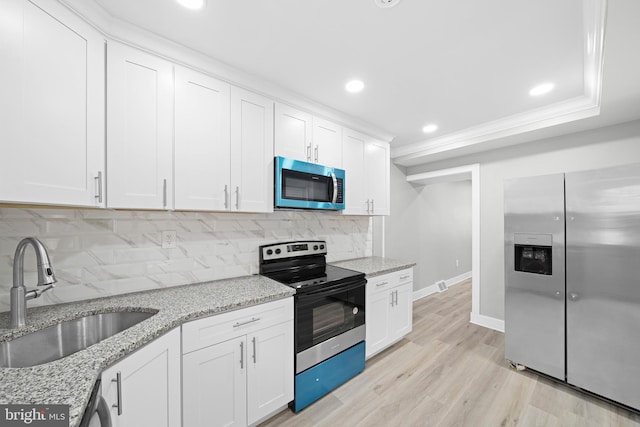 kitchen with light wood-type flooring, a sink, backsplash, appliances with stainless steel finishes, and white cabinets