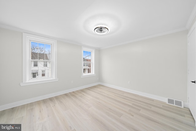 spare room with light wood-style floors, visible vents, crown molding, and baseboards