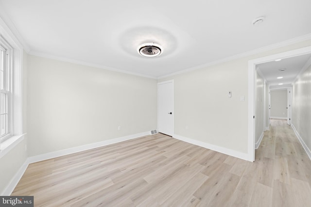 empty room with crown molding, light wood-style flooring, visible vents, and baseboards