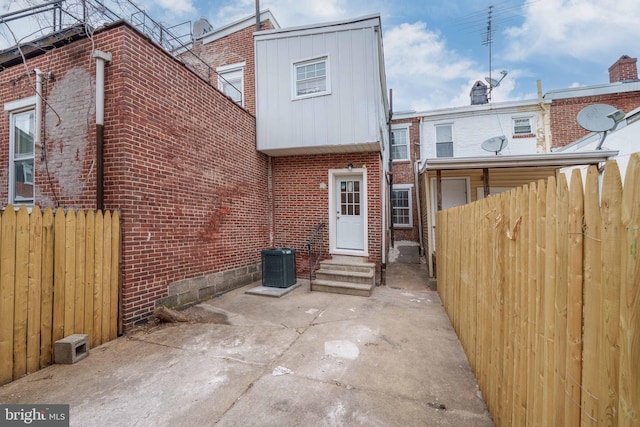 rear view of house featuring entry steps, fence, brick siding, central AC unit, and a patio area