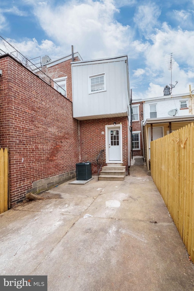 back of house with brick siding, fence, entry steps, central AC unit, and a patio area