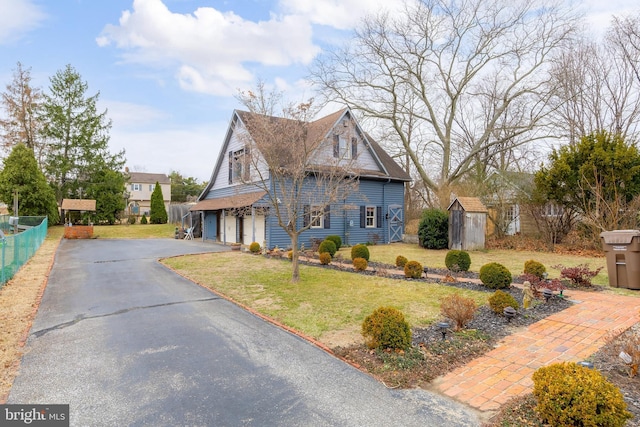 view of front of property featuring a front yard, fence, an attached garage, a storage unit, and aphalt driveway