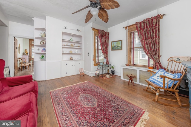 sitting room with built in features, baseboards, ceiling fan, and hardwood / wood-style flooring