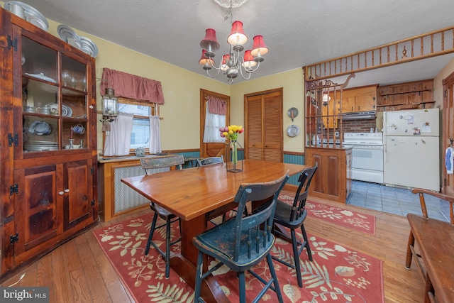 dining space with a chandelier, wainscoting, a textured ceiling, and wood finished floors