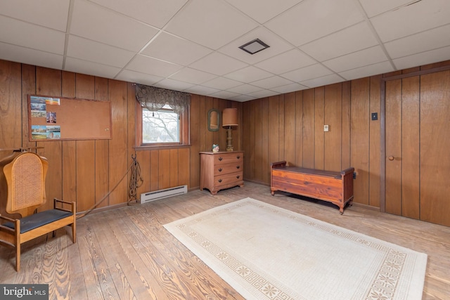 living area featuring wooden walls, light wood-type flooring, a baseboard heating unit, and a drop ceiling