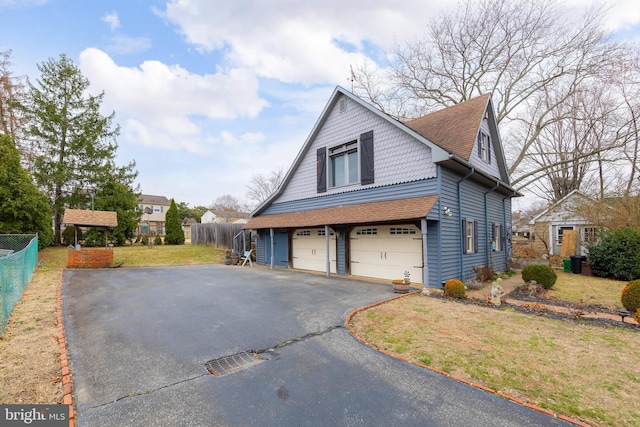 view of side of home featuring fence, aphalt driveway, roof with shingles, a lawn, and a garage