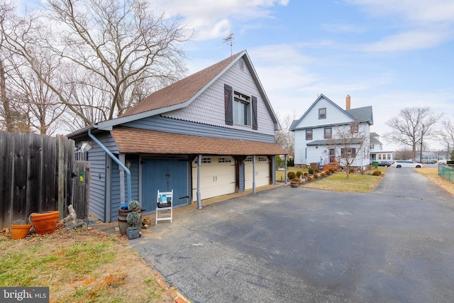 view of side of home with a garage, roof with shingles, driveway, and fence