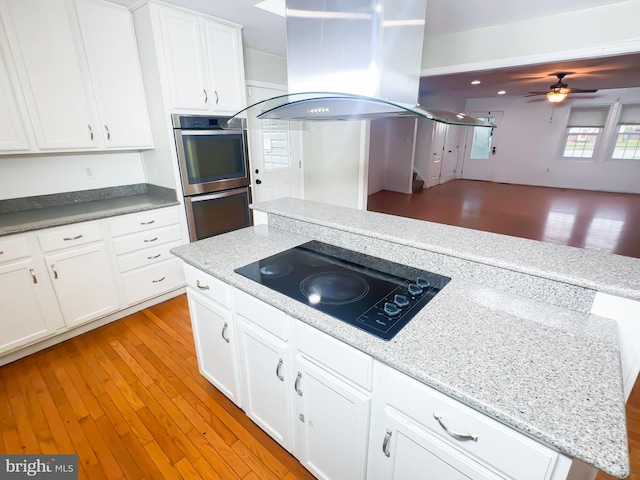 2204 Holly Oak Ct, Waldorf, MD 20601 - kitchen featuring black electric cooktop, ceiling fan, double oven, white cabinetry, and island range hood