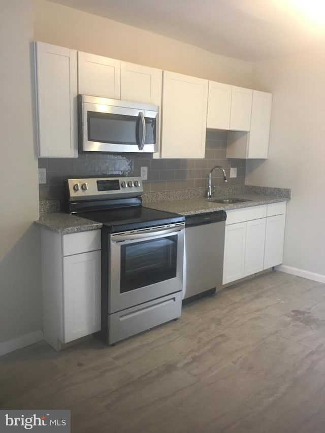 kitchen featuring tasteful backsplash, white cabinets, appliances with stainless steel finishes, and a sink