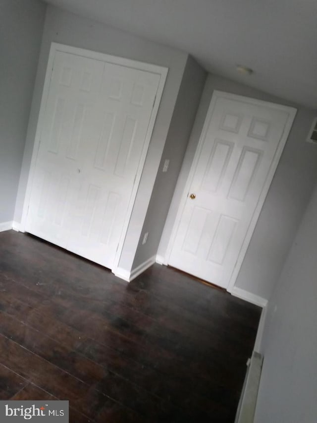 unfurnished bedroom featuring dark wood-type flooring, visible vents, and baseboards