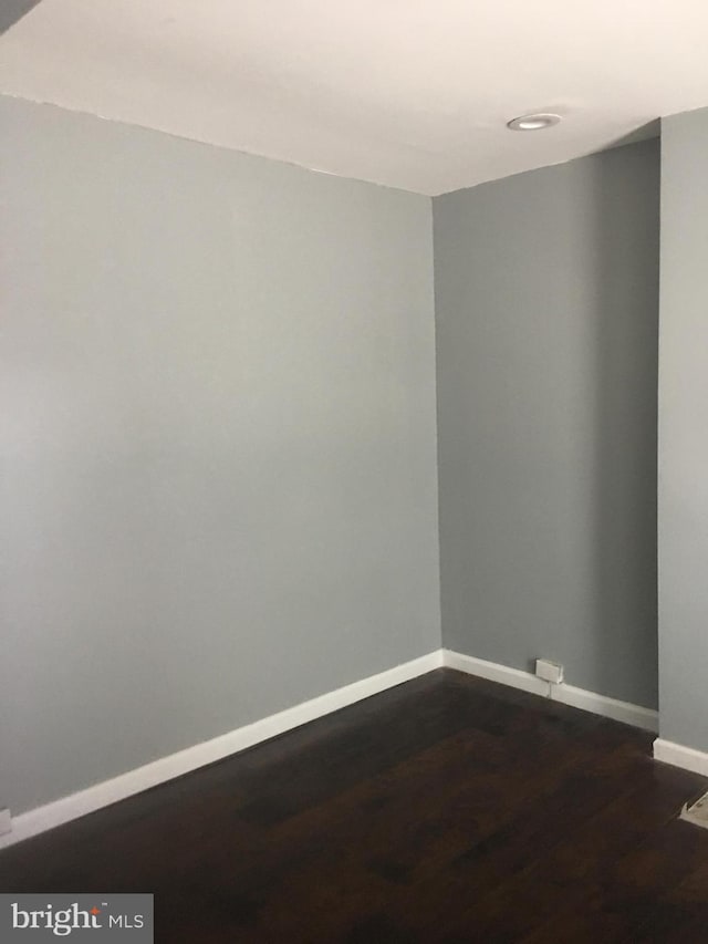 spare room featuring baseboards and dark wood-type flooring