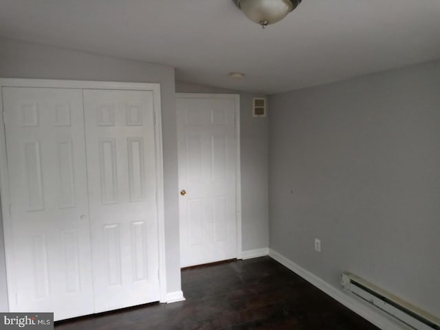 unfurnished bedroom featuring visible vents, a baseboard heating unit, baseboards, a closet, and dark wood-style flooring