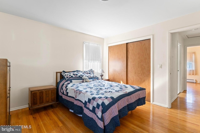 bedroom featuring a closet, light wood-style flooring, a baseboard heating unit, and baseboards