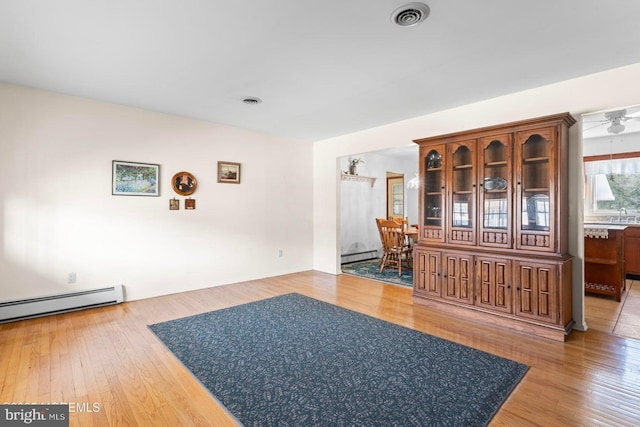 interior space with visible vents, a baseboard heating unit, hardwood / wood-style floors, a ceiling fan, and a baseboard radiator