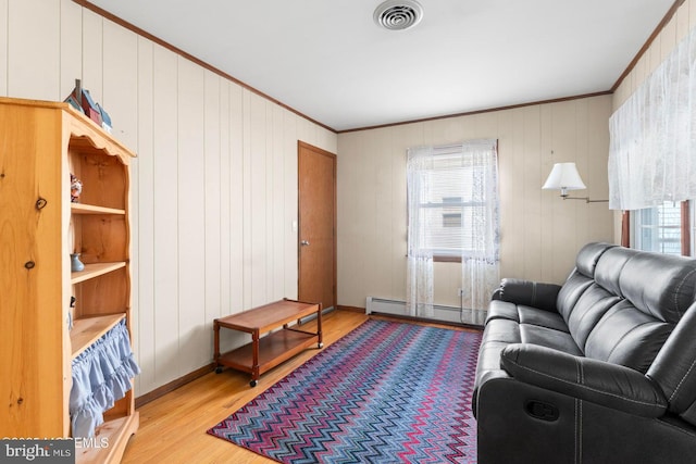 living room with a baseboard heating unit, wood finished floors, visible vents, and ornamental molding