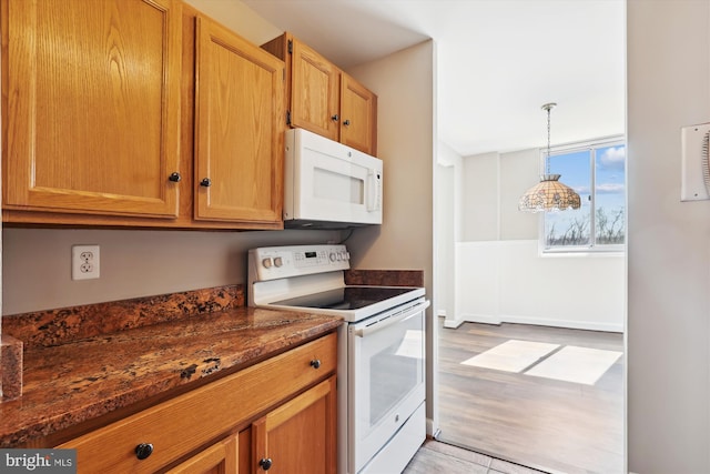 kitchen with pendant lighting, light wood-style flooring, dark stone counters, white appliances, and brown cabinetry