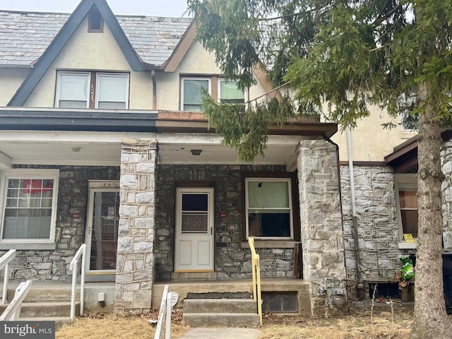 view of front of house with a porch, stone siding, and stucco siding