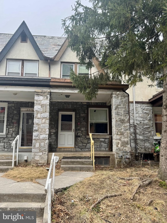 view of front of property featuring a porch, stone siding, and stucco siding