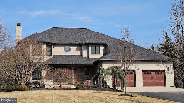 view of front of property featuring a front yard, an attached garage, a shingled roof, a chimney, and aphalt driveway