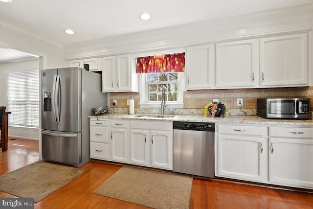 kitchen with a sink, white cabinetry, appliances with stainless steel finishes, crown molding, and decorative backsplash