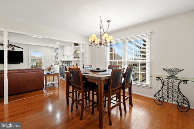 dining room with hardwood / wood-style floors, an inviting chandelier, a fireplace, and baseboards