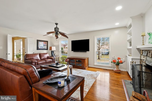 living room featuring wood finished floors, recessed lighting, a stone fireplace, baseboards, and ceiling fan