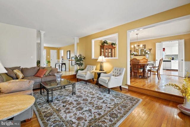 living area featuring ornate columns, plenty of natural light, a notable chandelier, and light wood finished floors