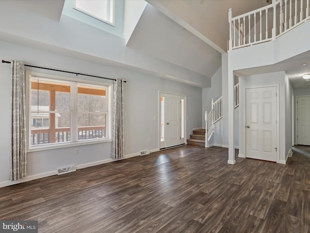 unfurnished living room featuring visible vents, baseboards, stairs, a high ceiling, and wood finished floors