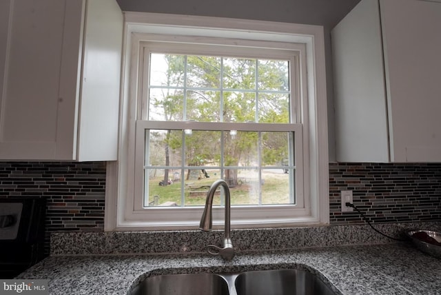 kitchen featuring white cabinetry, decorative backsplash, light stone counters, and a sink