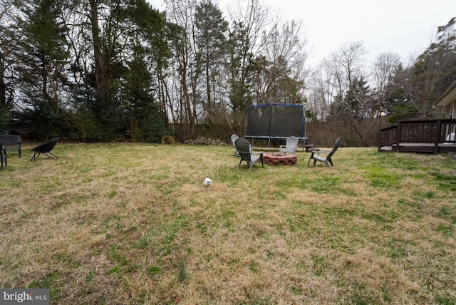 view of yard featuring a trampoline, a deck, and an outdoor fire pit