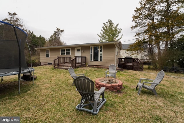 back of property featuring a wooden deck, a yard, an outdoor fire pit, and a trampoline