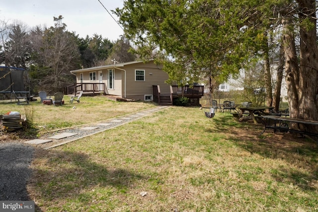 view of yard featuring a fire pit, a wooden deck, and a trampoline